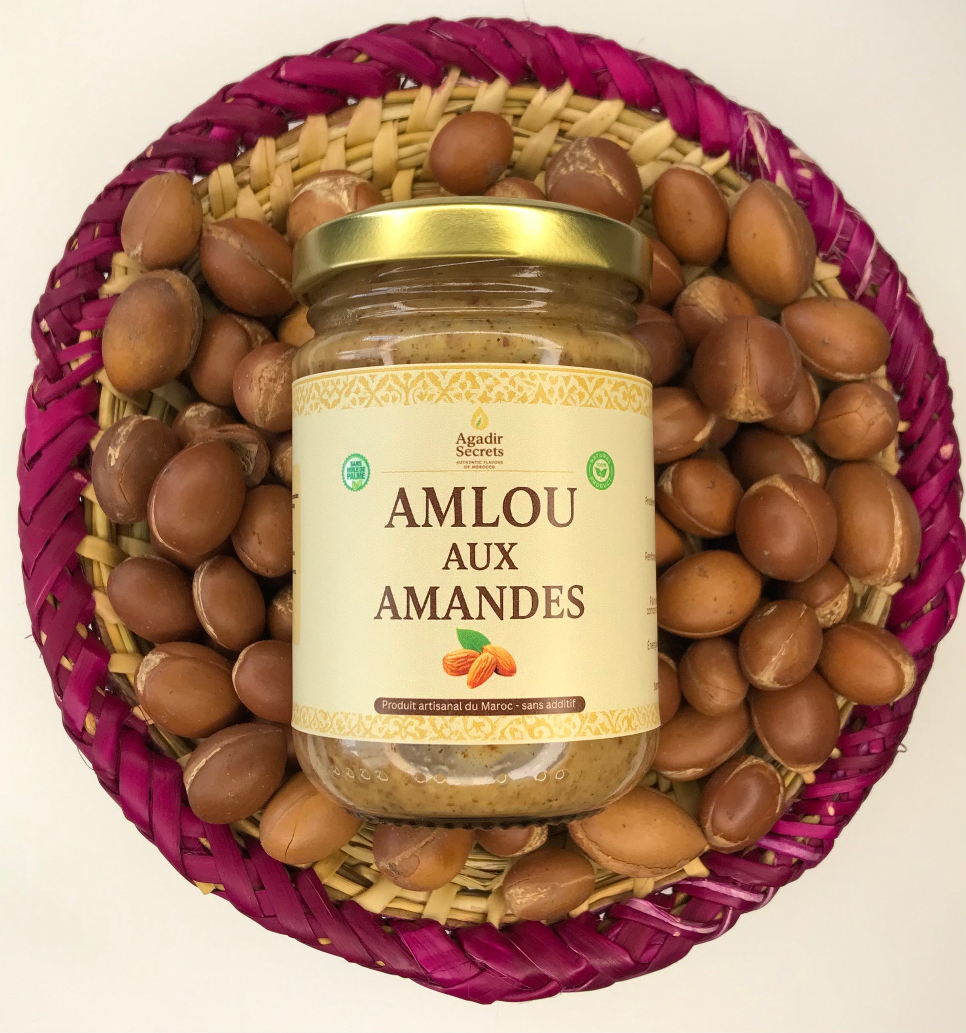 Pot en verre d'Amlou aux amandes artisanal Agadir Secrets, posé sur des noix d'argan marocaines dans un panier tressé. Préparé et expédié depuis Bruxelles, Belgique.